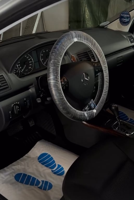Mercedes-Benz car interior with steering wheel wrapped in clear plastic protection and white protective seat covers