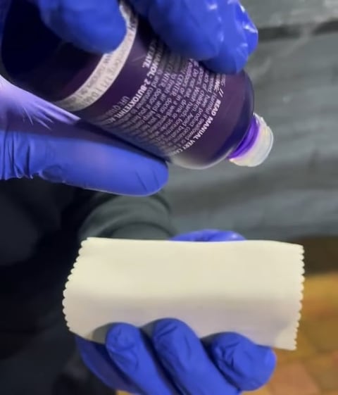 Gloved hands holding a dark labeled bottle above a white absorbent material