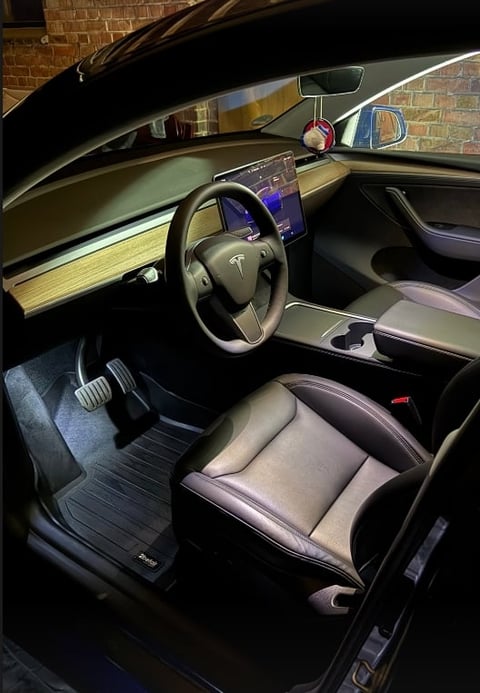 Interior of a Tesla vehicle with wood-trimmed dashboard and panoramic roof