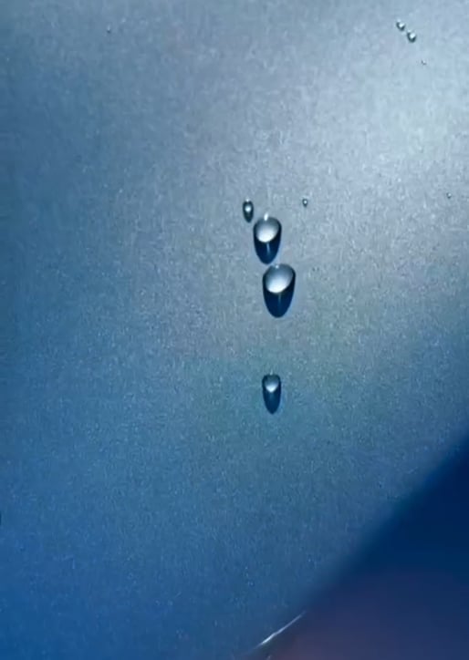Water droplets suspended on a blue textured surface with light reflection