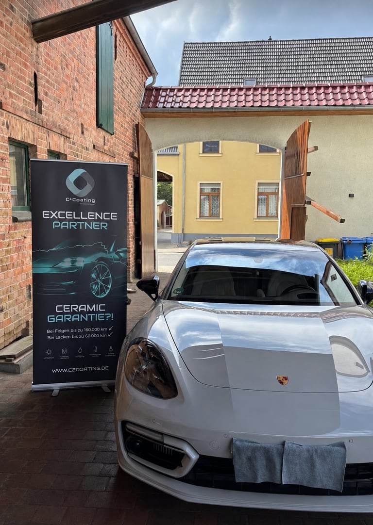 White Porsche sports car parked next to a C-Coating Excellence Partner ceramic garage sign